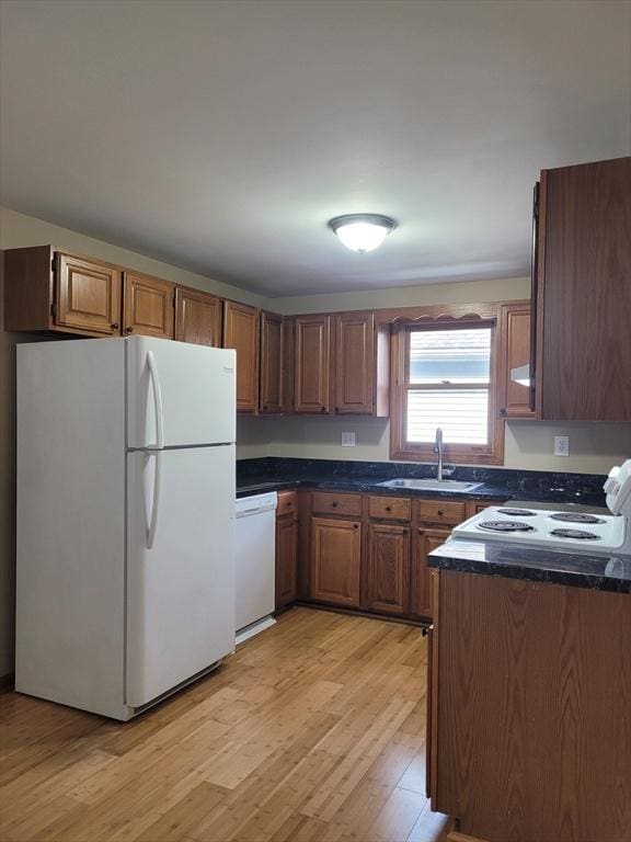 kitchen with white appliances, brown cabinetry, dark countertops, light wood-style flooring, and a sink