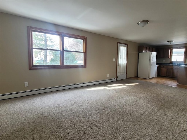 unfurnished living room featuring light carpet, baseboard heating, and a sink