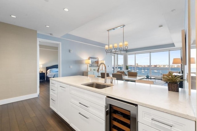 kitchen with wine cooler, sink, decorative light fixtures, light stone countertops, and white cabinets