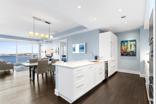 kitchen with sink, a water view, decorative light fixtures, dark hardwood / wood-style floors, and white cabinets