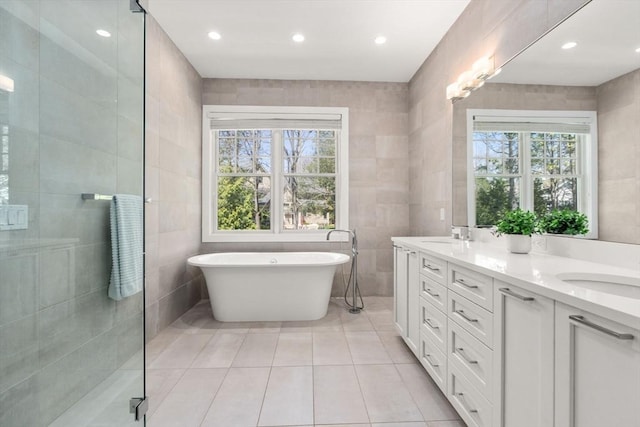 bathroom with double vanity, tile walls, a freestanding bath, tile patterned floors, and a sink
