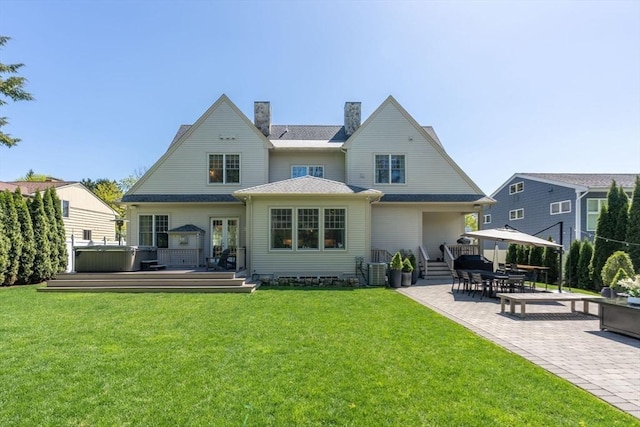 rear view of property with a wooden deck, a chimney, a patio area, a lawn, and a hot tub