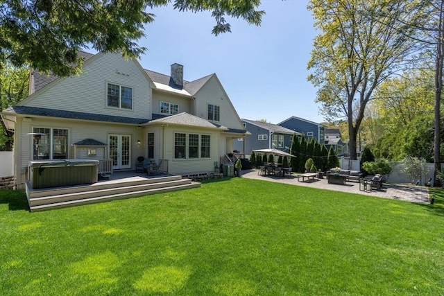 back of property with a hot tub, a chimney, a patio area, french doors, and a yard