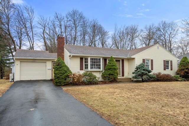 ranch-style home featuring an attached garage, a shingled roof, a chimney, a front lawn, and aphalt driveway