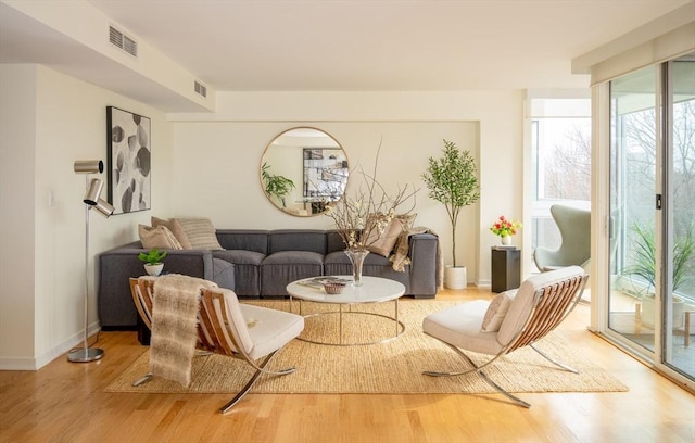 living area featuring light wood-type flooring, visible vents, baseboards, and expansive windows