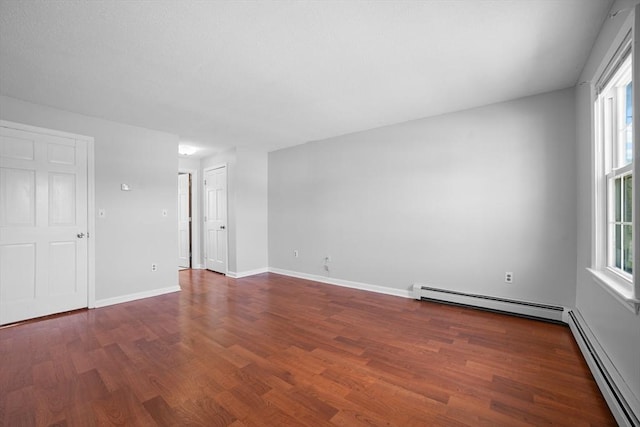 spare room with a healthy amount of sunlight, baseboard heating, a baseboard heating unit, and wood finished floors