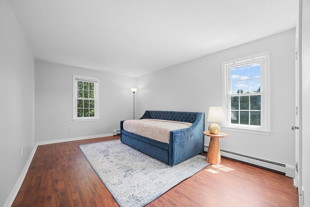 bedroom with wood finished floors, baseboards, baseboard heating, and a baseboard radiator