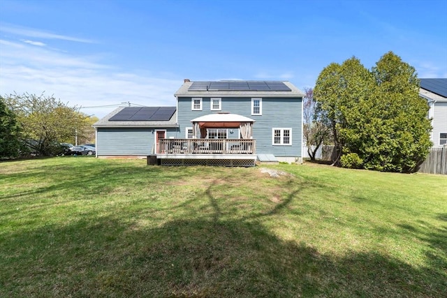 back of property with a yard, a gazebo, a wooden deck, and roof mounted solar panels