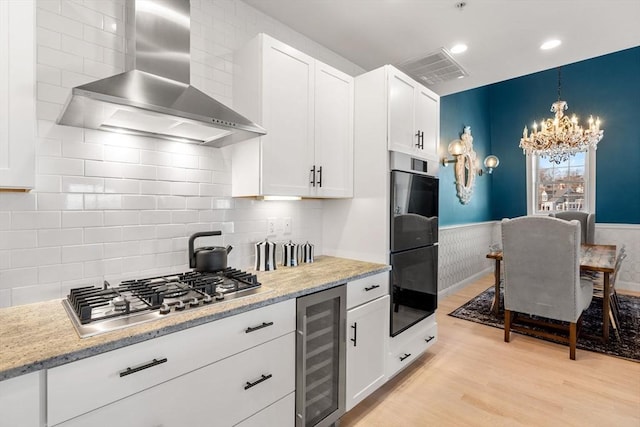 kitchen featuring beverage cooler, stainless steel gas cooktop, wainscoting, wall chimney exhaust hood, and light wood-type flooring