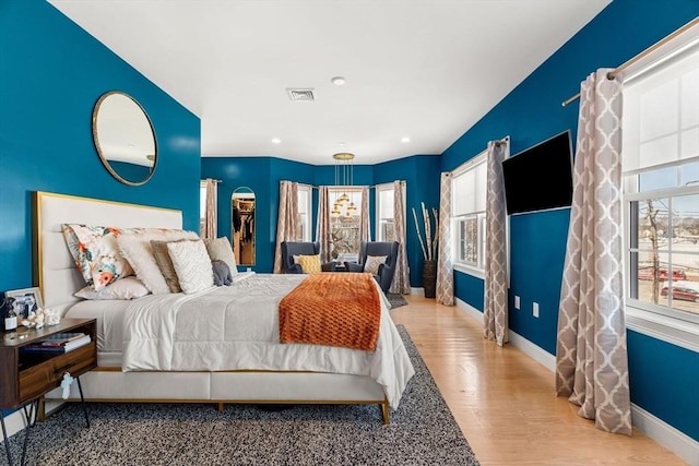 bedroom featuring visible vents, multiple windows, baseboards, and wood finished floors