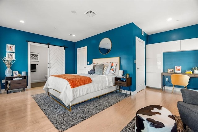 bedroom with a barn door, baseboards, visible vents, and wood finished floors