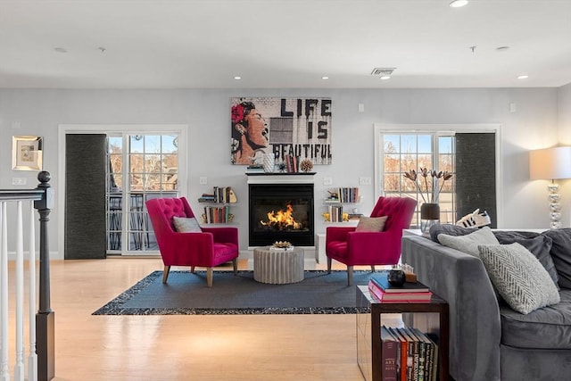 living room with a glass covered fireplace, a healthy amount of sunlight, and wood finished floors