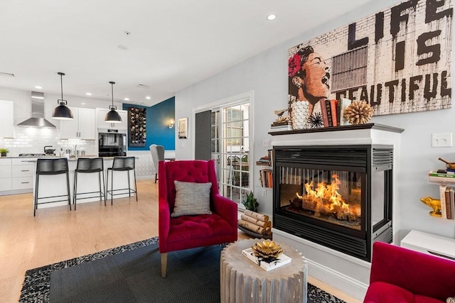 sitting room with a multi sided fireplace, recessed lighting, and light wood-style floors