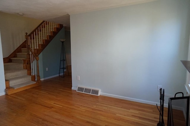 unfurnished living room with visible vents, stairs, baseboards, and wood finished floors