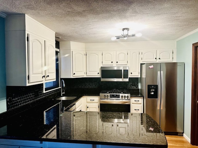 kitchen featuring dark stone countertops, appliances with stainless steel finishes, a peninsula, white cabinets, and a sink