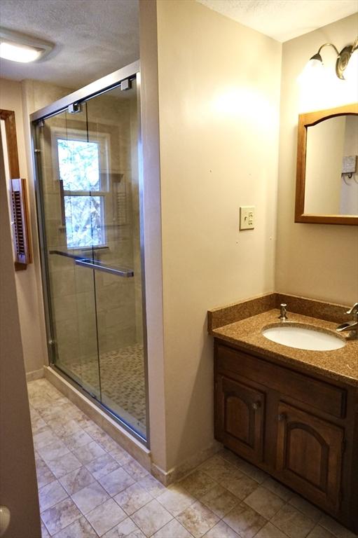 bathroom with a stall shower, a textured ceiling, vanity, and baseboards