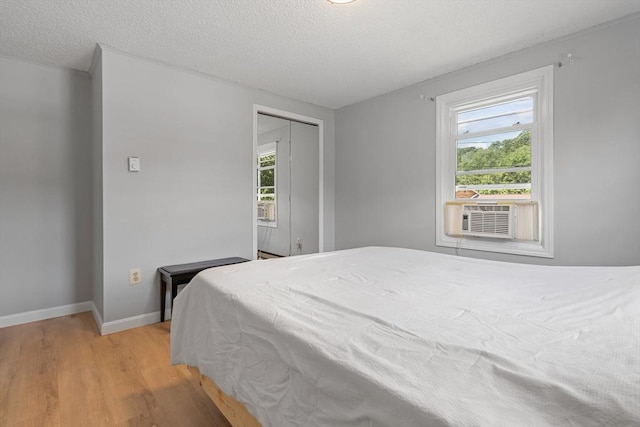 bedroom with cooling unit, a textured ceiling, light wood-type flooring, and a closet