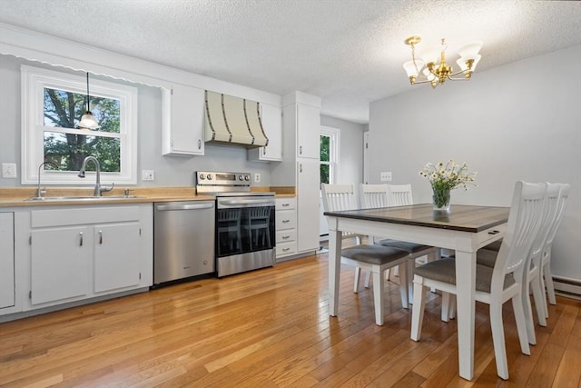 kitchen with sink, appliances with stainless steel finishes, hanging light fixtures, white cabinets, and exhaust hood