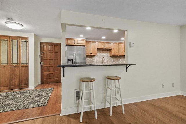 9 Broadway Unit 217, Saugus, MA 01906 - kitchen with stainless steel refrigerator with ice dispenser, dark countertops, wood finished floors, a kitchen breakfast bar, and backsplash