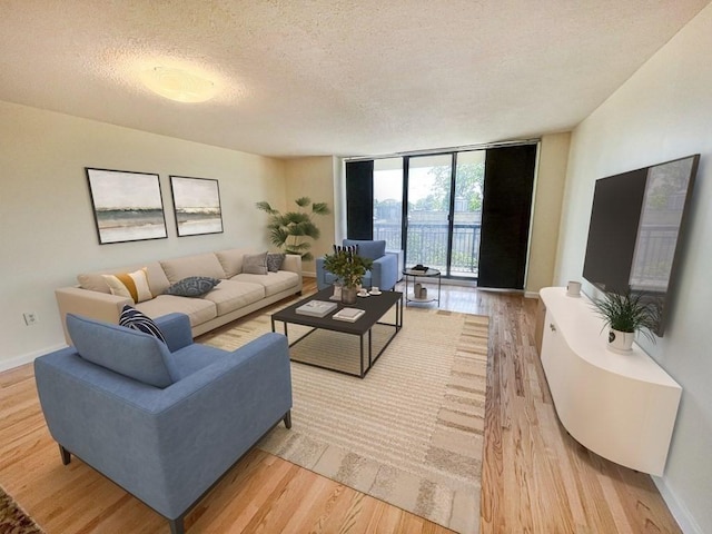 living area with a wall of windows, light wood-style floors, a textured ceiling, and baseboards