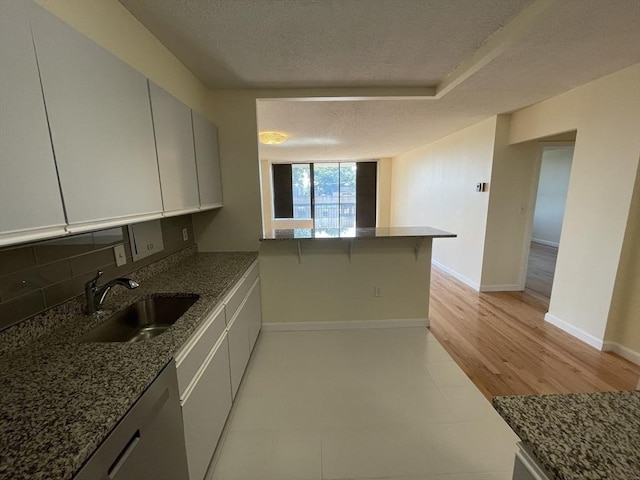 kitchen featuring backsplash, a sink, a textured ceiling, dark stone counters, and baseboards