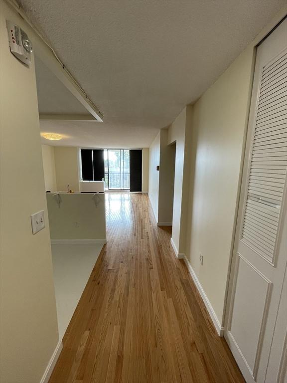 hallway featuring floor to ceiling windows, a textured ceiling, baseboards, and wood finished floors