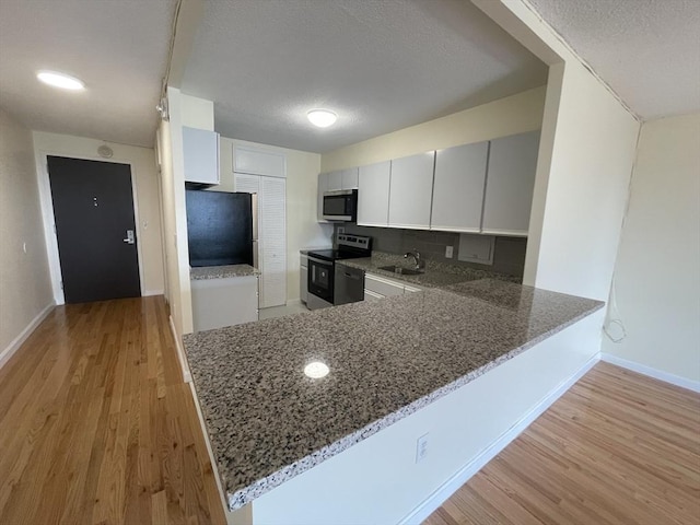 kitchen featuring light wood finished floors, appliances with stainless steel finishes, light stone countertops, a peninsula, and baseboards