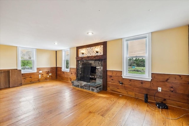 unfurnished living room with light wood-style floors, wainscoting, wooden walls, and a fireplace
