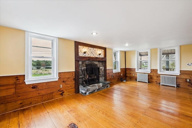 living room featuring radiator, a wainscoted wall, a stone fireplace, and wood finished floors