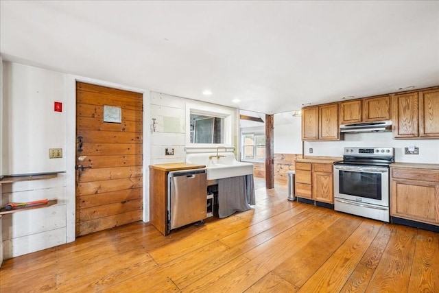 kitchen with brown cabinetry, light wood-style floors, light countertops, under cabinet range hood, and stainless steel appliances
