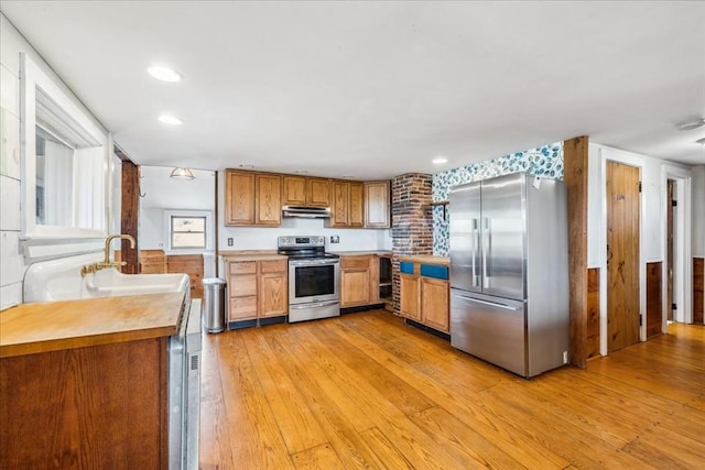 kitchen with brown cabinetry, a sink, light countertops, light wood-style floors, and stainless steel appliances