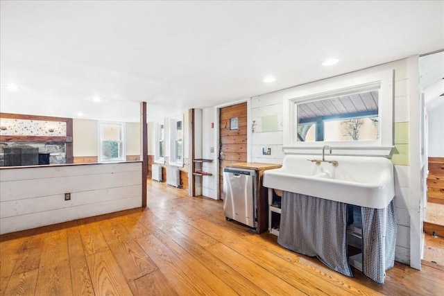 kitchen with light wood-style floors, stainless steel dishwasher, a fireplace, and wood walls