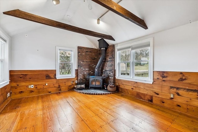 interior space with a wood stove, hardwood / wood-style floors, wooden walls, a wainscoted wall, and lofted ceiling with beams