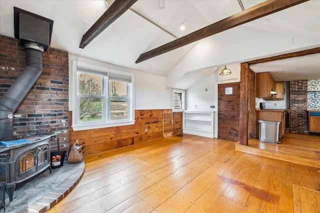 living room with light wood-type flooring, a wood stove, lofted ceiling with beams, and a wainscoted wall