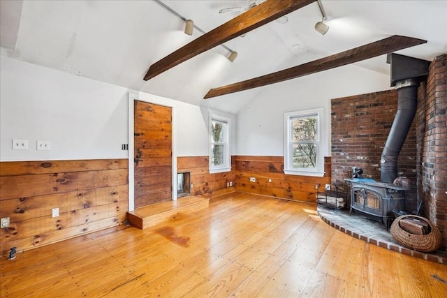 living area featuring a wood stove, wood walls, hardwood / wood-style floors, a wainscoted wall, and vaulted ceiling with beams