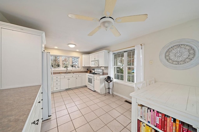 kitchen with white appliances, ceiling fan, sink, light tile patterned floors, and white cabinetry