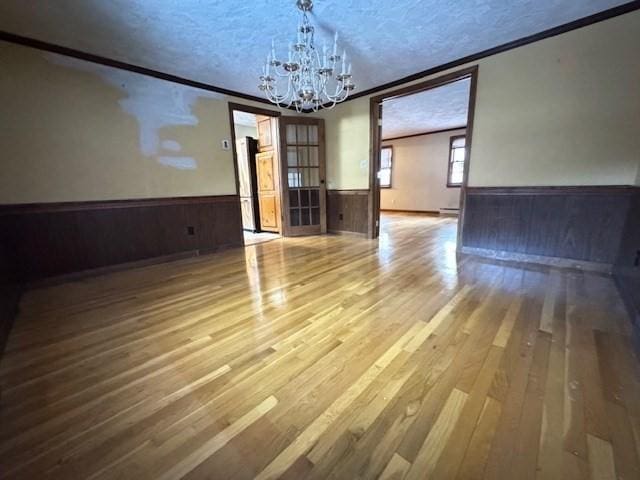 unfurnished dining area featuring wood walls, wood-type flooring, a notable chandelier, crown molding, and a textured ceiling