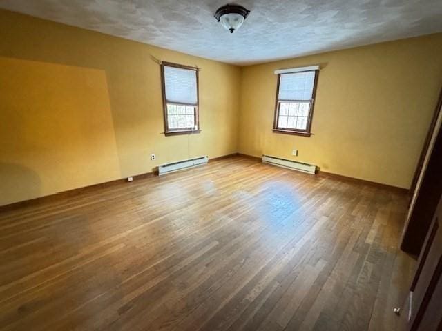 empty room featuring a wealth of natural light, a baseboard radiator, and hardwood / wood-style flooring