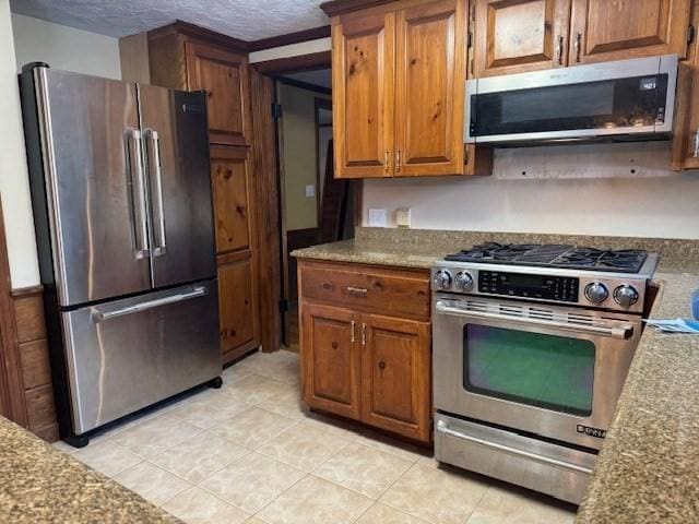 kitchen featuring stainless steel appliances, light stone countertops, light tile patterned floors, and a textured ceiling