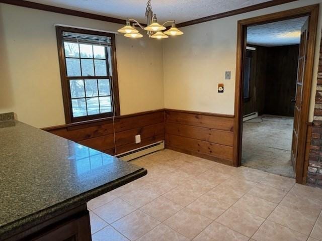 unfurnished dining area featuring baseboard heating, ornamental molding, wooden walls, and a notable chandelier