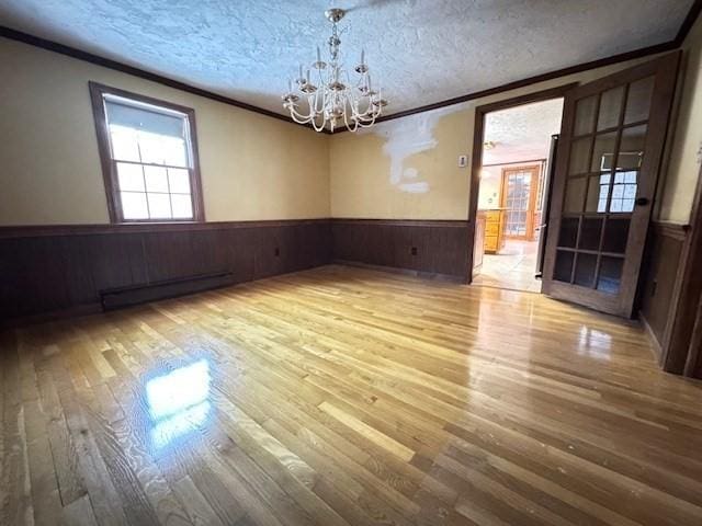 unfurnished dining area featuring baseboard heating, an inviting chandelier, hardwood / wood-style floors, ornamental molding, and a textured ceiling