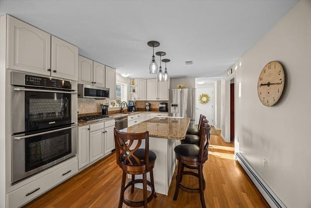 kitchen featuring light stone countertops, a sink, appliances with stainless steel finishes, a baseboard heating unit, and backsplash