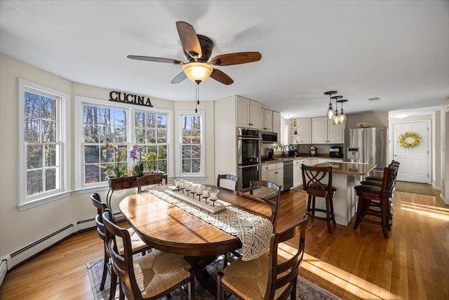 dining space featuring baseboard heating, a ceiling fan, and light wood-style floors