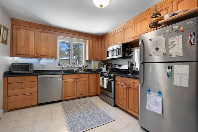 kitchen featuring a toaster, dark countertops, appliances with stainless steel finishes, brown cabinetry, and a sink