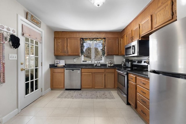 kitchen with stainless steel appliances, brown cabinetry, dark countertops, and a sink