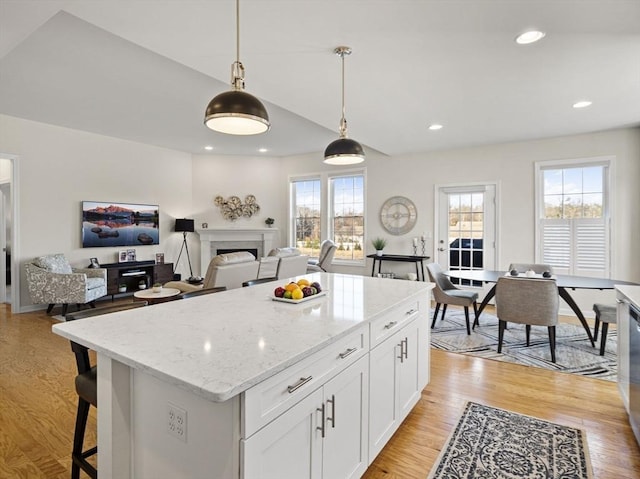 kitchen featuring decorative light fixtures, white cabinets, a kitchen island, light hardwood / wood-style flooring, and light stone counters