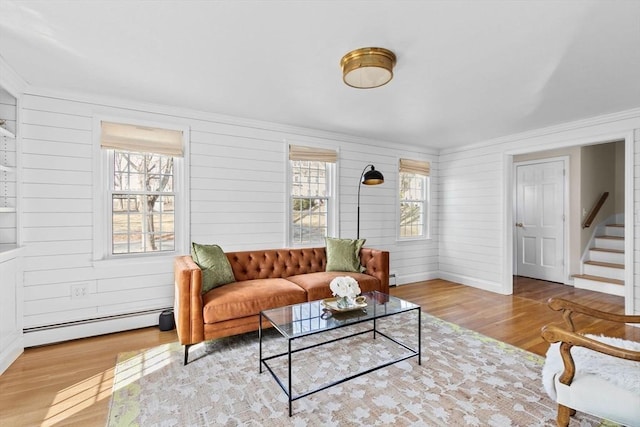 living area with a baseboard heating unit, baseboards, wood finished floors, and stairs