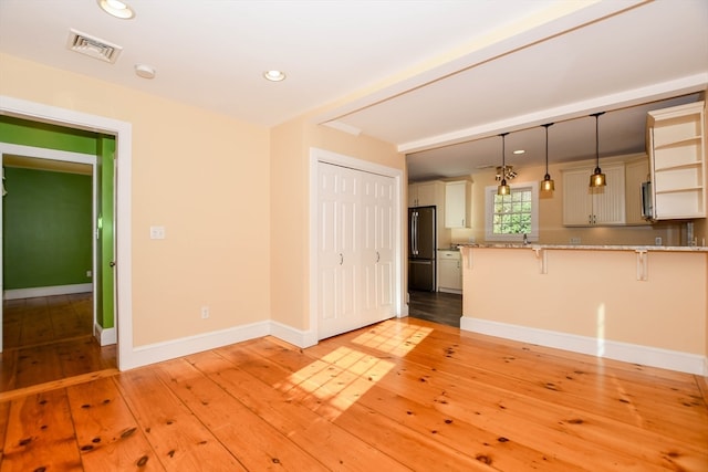 kitchen with a breakfast bar area, light hardwood / wood-style flooring, hanging light fixtures, kitchen peninsula, and stainless steel refrigerator