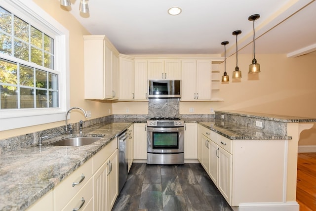 kitchen featuring light stone countertops, appliances with stainless steel finishes, sink, kitchen peninsula, and decorative light fixtures