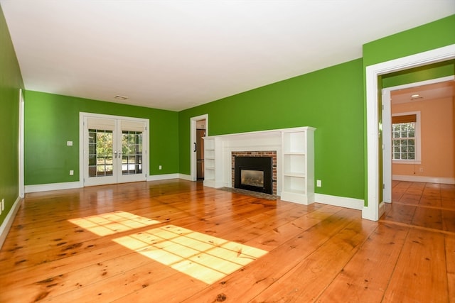 unfurnished living room with french doors, light wood-type flooring, and a brick fireplace